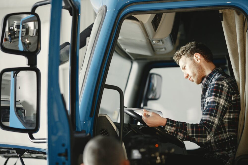 man in plaid shirt sitting in the body of blue truck and reading papers